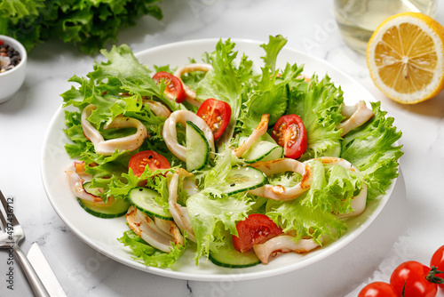 Green salad with grilled squid or calamari with tomatoes, cucumber on white plate.