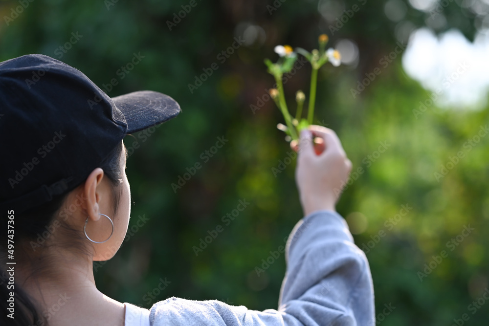 Rear view of young woman hand holding young plant on blur green nature background. Earth day concept.