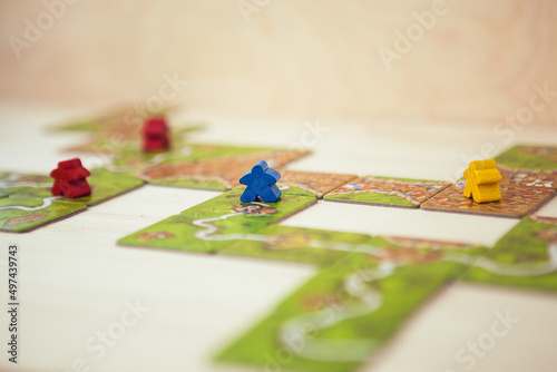 Carcassonne board game, game cards and colored chips on wooden table. Carcassonne boad game components, colorful field, tiles and meeples. Family game