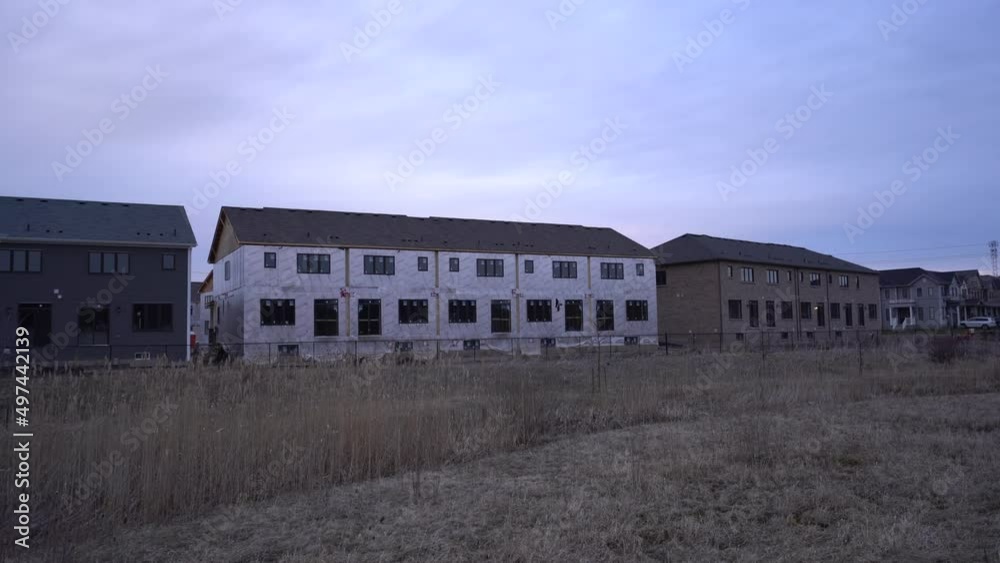 Wide pan of town houses with insulation exposed under construction by builder during dry overcast winter day - Unfinished towns - New town homes real estate building through builder in Ontario, Canada Wide pan of town houses with insulation exposed under construction by builder during dry overcast winter day - Unfinished towns - New town homes real estate building through builder in Ontario, Canada