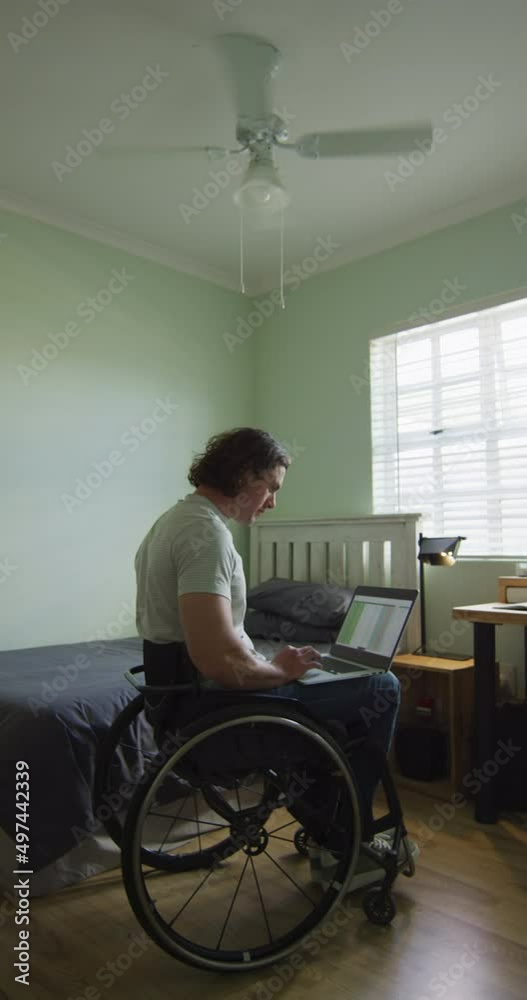 Vertical video of caucasian disabled man sitting in wheelchair using laptop Vertical video of caucasian disabled man sitting in wheelchair using laptop