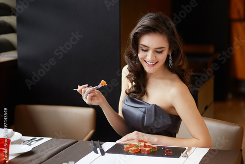 Sensual brunette in an evening dress, serves a dessert in the restaurant, dressed in a dress with bare shoulders, makeup and hairstyle.