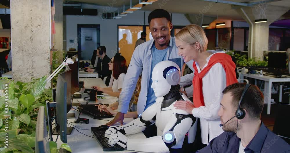 Happy mixed-races people standing and looking at humanoid working in office. Robot typing on keyboard at call center. Support service of future. Men and women cheering up for android.