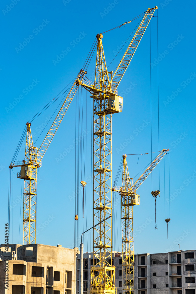 Three high construction tower cranes against the blue sky. Construction of a multi-storey building.