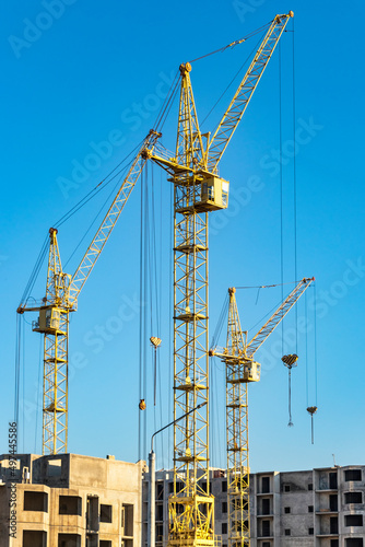 Three high construction tower cranes against the blue sky. Construction of a multi-storey building. © Anoo