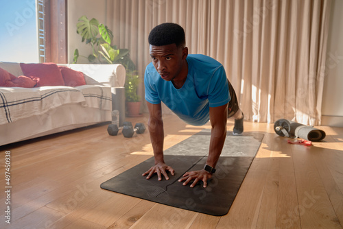 African American male holding high plank in living room, exercising at home