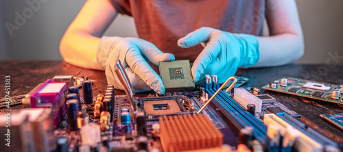 Engineer's gloved hand is holding the CPU chip on the background of the motherboard. High-tech hardware microelectronics photo