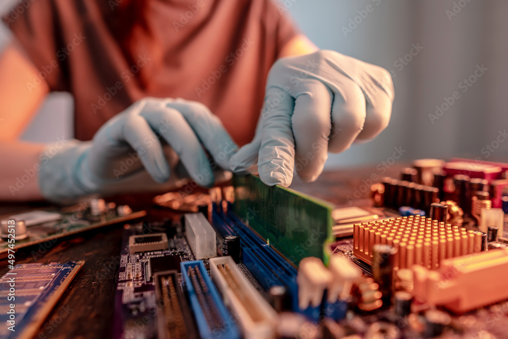 The engineer's gloved hand holds the computer's RAM chip against the background of the motherboard