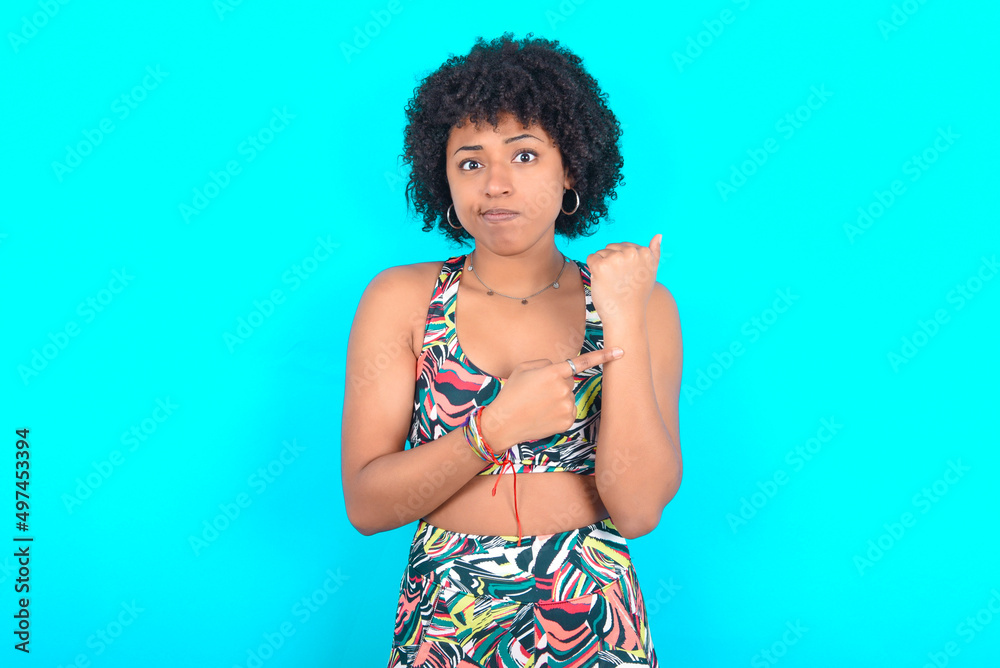 young woman with afro hairstyle in sportswear against blue background in hurry pointing to watch time, impatience, upset and angry for deadline delay young woman with afro hairstyle in sportswear against blue background in hurry pointing to watch time, impatience, upset and angry for deadline delay