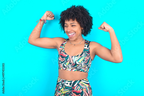 Yes I am winner. Portrait of charming delighted and excited young woman with afro hairstyle in sportswear raising up fist in triumph and victory smiling achieving success grinning from delight. © Jihan