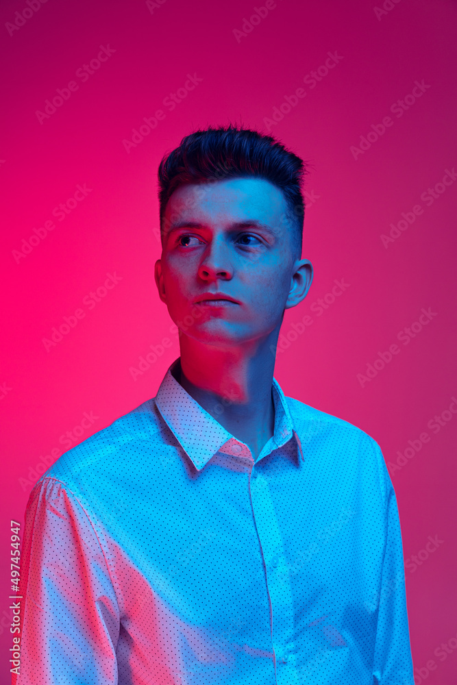 Obraz premium Half-length portrait of young handsome man in white shirt posing isolated over magenta color studio background in blue neon light
