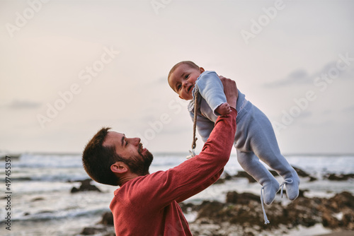 Young single father lifting his baby and playing with him on the beach