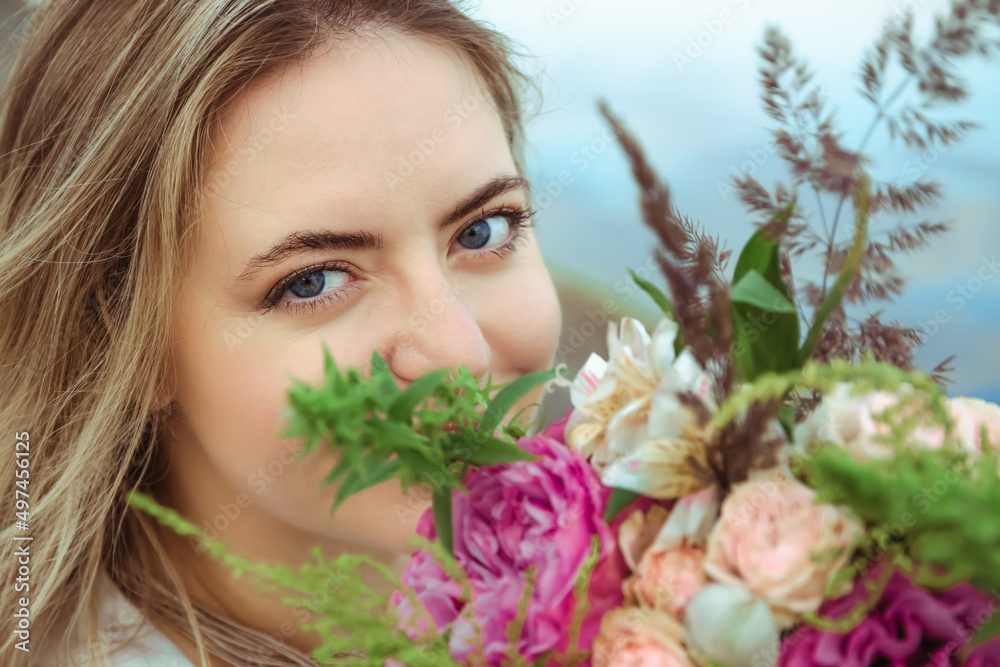 Portrait of young beautiful woman caucasian appearance smiling and looking at camera through the lush flowers bouquet. Happy summer mood. Attractive girl lifestyle. Big blue lady eyes. Flirting look