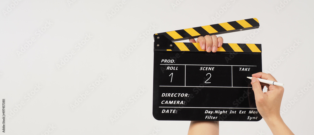 The hand is holding a yellow and black clapper board and a marker Pen with a written number on the clapper board on black background.