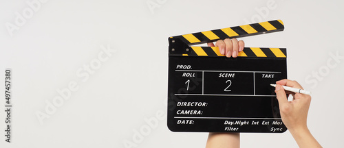 The hand is holding a yellow and black clapper board and a marker Pen with a written number on the clapper board on black background.