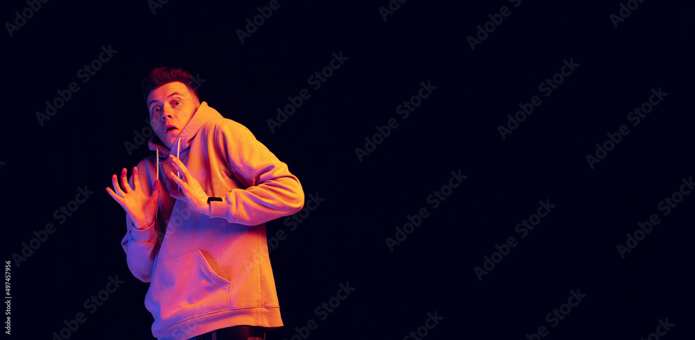 Flyer with young scared man wearing hoodie isolated over dark studio background in neon light. Concept of emotions, fashion, psychology Flyer with young scared man wearing hoodie isolated over dark studio background in neon light. Concept of emotions, fashion, psychology
