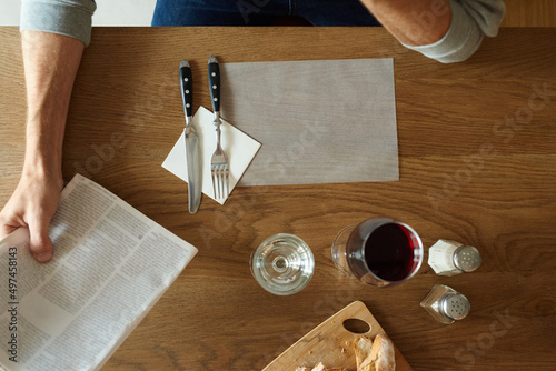 Man's arm with magazine at table with wine.