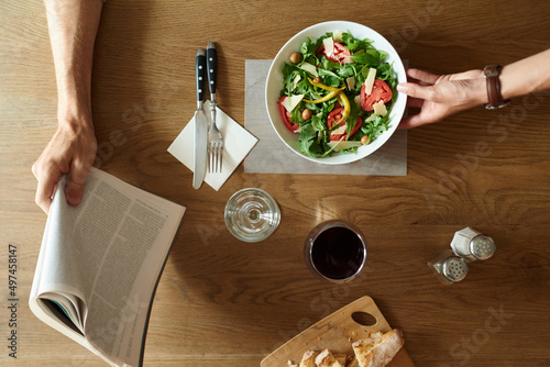 Waitress brings fresh salad on table with man's arm with magazine.