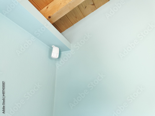 Motion sensor or detector for security system mounted on blue wall in mansard room with wooden ceiling photo