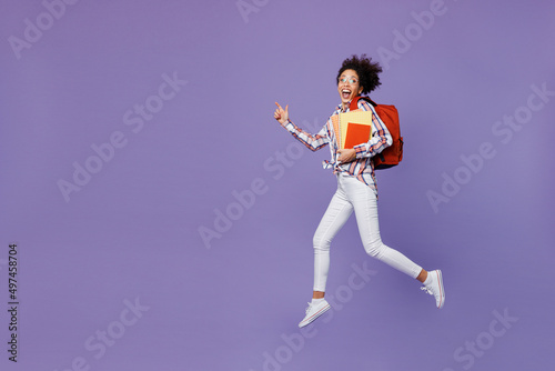 Full body excited happy young girl woman of African American ethnicity teen student in shirt hold backpack jump high hurry up run fast isolated on plain purple background Education in college concept