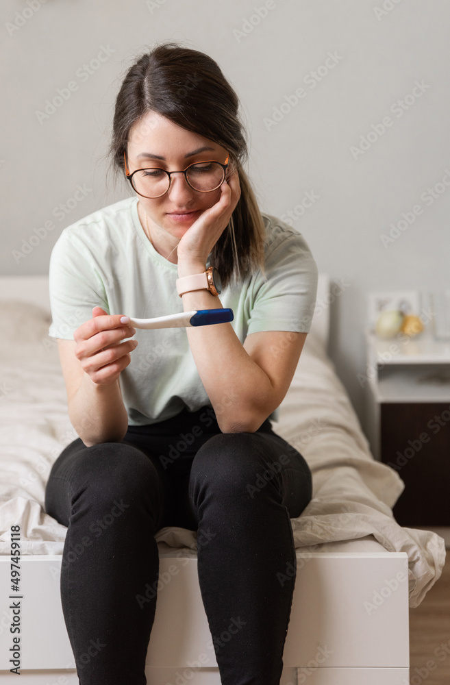 the woman found out about an unwanted pregnancy. A woman with a pregnancy test in her hands is sitting on the bed in her apartment the woman found out about an unwanted pregnancy. A woman with a pregnancy test in her hands is sitting on the bed in her apartment