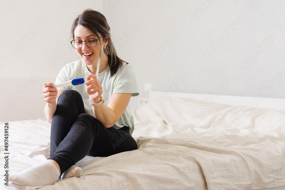 a woman looks at a pregnancy test sitting on the bed. The woman is happy and rejoices in pregnancy. A woman at home found out that she was pregnant a woman looks at a pregnancy test sitting on the bed. The woman is happy and rejoices in pregnancy. A woman at home found out that she was pregnant
