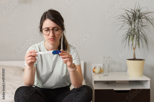 a woman with a pregnancy test in her hands is sitting on the bed. The girl found out about an unwanted pregnancy.