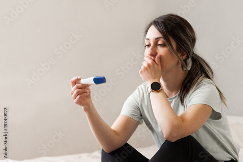 the woman found out about an unwanted pregnancy. A woman with a pregnancy test in her hands is sitting on the bed in her apartment photo