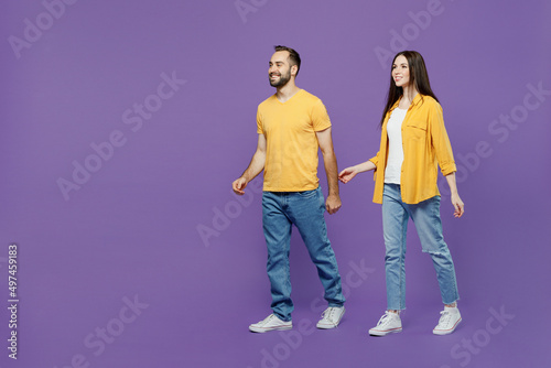 Full body side view young couple two friends family man woman together wearing yellow casual clothes looking to each other hold hands walking going stroll isolated on plain violet background studio