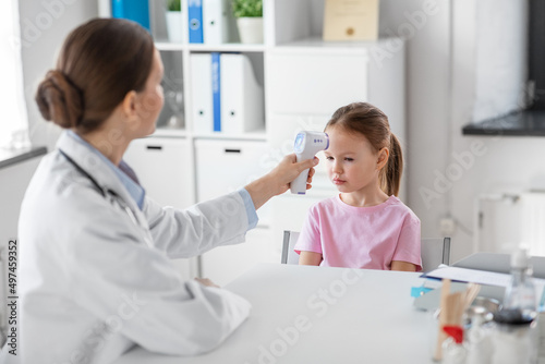 medicine  healthcare and pediatry concept - female doctor or pediatrician measuring little girl patient s temperature with infrared forehead thermometer at clinic