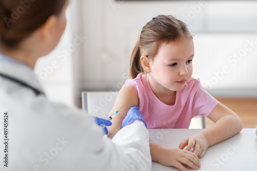 medicine, healthcare and vaccination concept - female doctor or pediatrician with syringe making vaccine injection to little girl patient at clinic