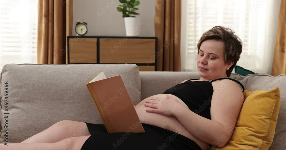 Happy pregnant woman touching her tummy at home. Pregnant woman resting on sofa, carresing her tummy