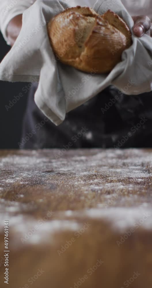 Vertical video of midsection of african american baker holding freshly baked loaf of bread in cloth Vertical video of midsection of african american baker holding freshly baked loaf of bread in cloth