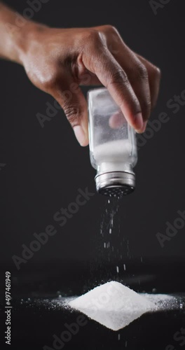 Vertical video of hand of african american man shaking salt from cellar into pile on black surface photo