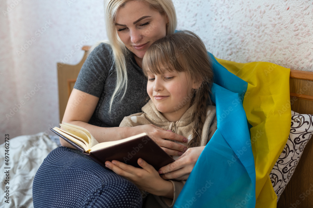 mother and daughter reading a book with the flag of ukraine in bed