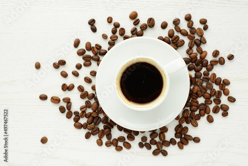 Cup of coffee with coffee beans on white wooden background. Top view