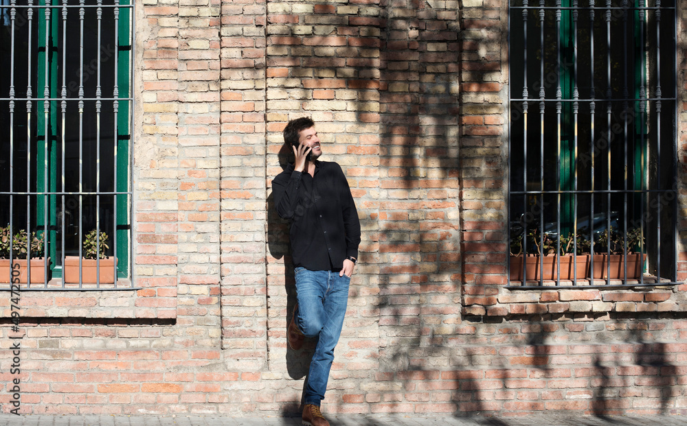 Bearded man leaning on a wall chatting on a mobile Bearded man leaning on a wall chatting on a mobile