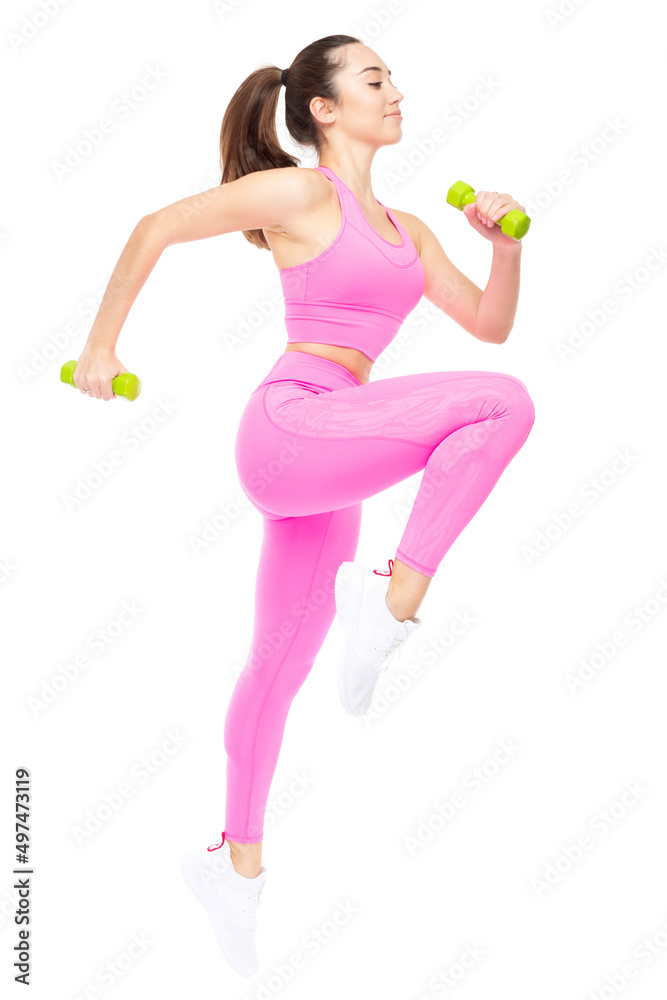 A beautiful, athletic, slim, smiling and cheerful woman in a pink tracksuit performs jumps with dumbbells. Lifestyle concept with sports and gym, moving towards the goal. Isolated on white background. A beautiful, athletic, slim, smiling and cheerful woman in a pink tracksuit performs jumps with dumbbells. Lifestyle concept with sports and gym, moving towards the goal. Isolated on white background.