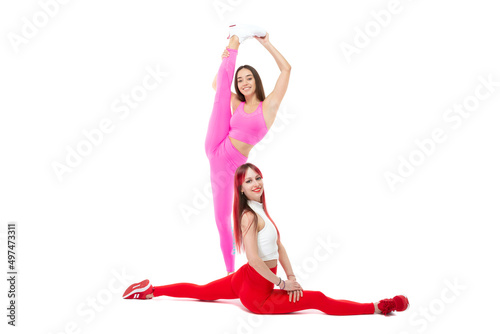 Two beautiful athletic slim smiling and cheerful women demonstrate stretching Sits on a split and stands with a raised leg Pilаtes Lifestyle concept with sports and gym Isolated on white background