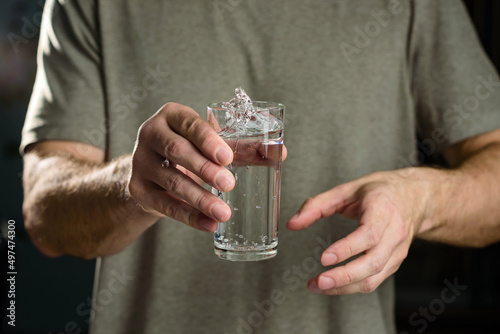 Tremor of the hands when trying to drink. Water splashes from a glass in the hand of a man with tremors, Parkinson's disease.