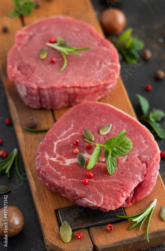 Raw beef fillet steaks with herbs and spices on wooden board on dark background close up