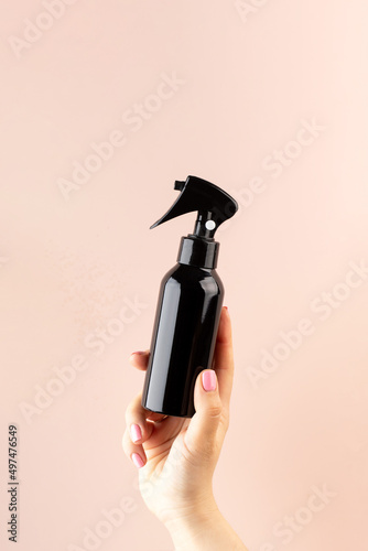 A mockup of a professional hair product in a brown pulvilizer in a woman's hand on a pink background.