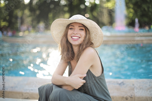 young smiling woman sitting on the edge of a fountain in a park
