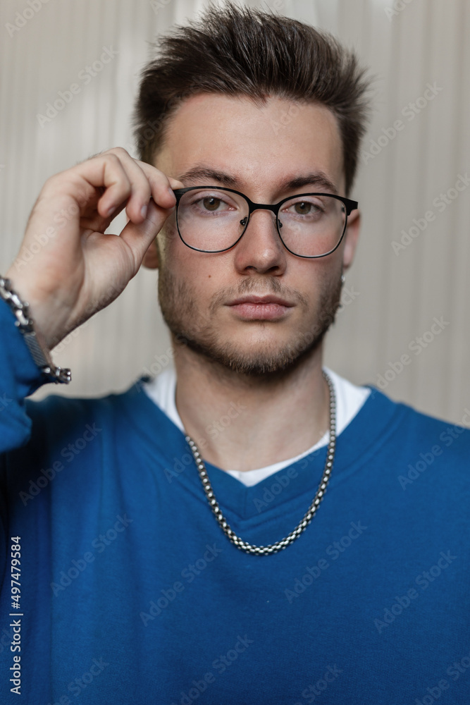 Obraz premium Stylish portrait of a handsome young hipster guy with hairstyle in a trendy blue sweater wearing glasses on the street