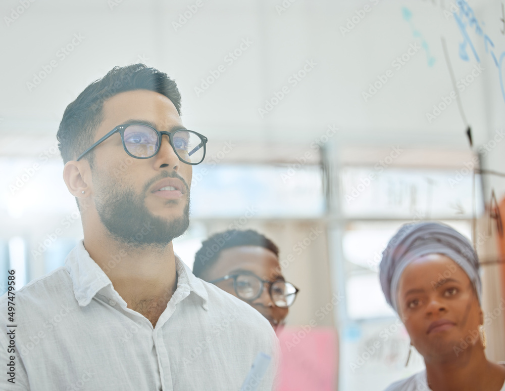 Obraz premium Focused on finding a winning strategy. Cropped shot of a group of diverse young businesspeople working on a glass wipe board in the boardroom.