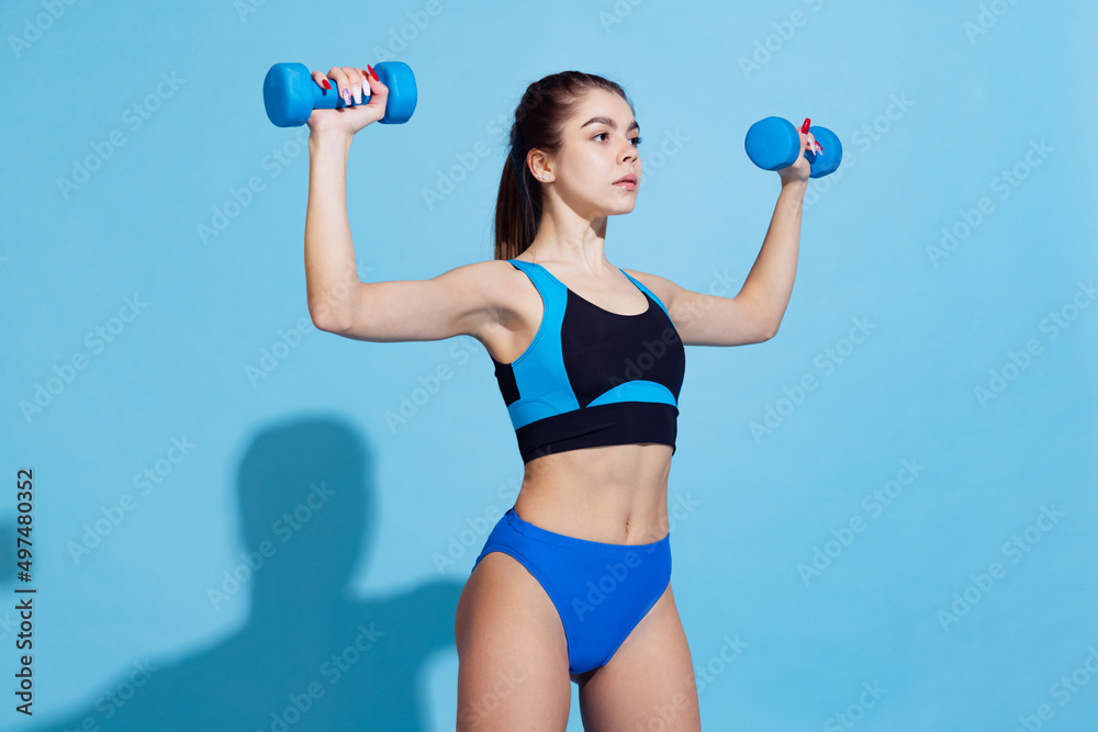 Young beautiful sportive girl training with sports equipment isolated on blue studio background. Sport, action, fitness, youth concept. Young beautiful sportive girl training with sports equipment isolated on blue studio background. Sport, action, fitness, youth concept.