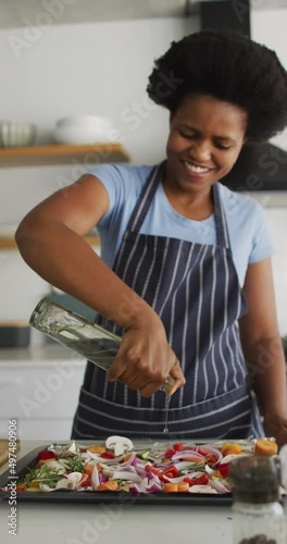 Vertical video of happy african american woman cooking at home photo