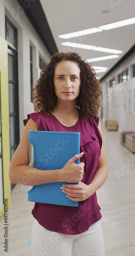 Vertical video of portrait of happy biracial female teacher looking at camera with documents