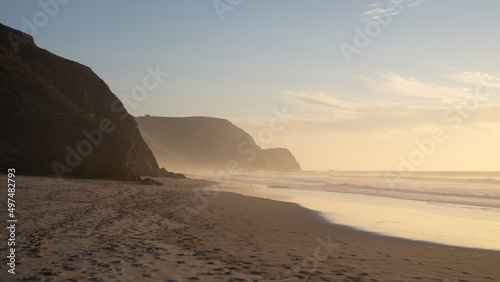 Fog in the ocean at sunset. Golden beach with mountains. Empty shore with mist. Brown coast in Portugal