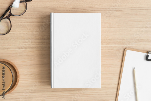 White book mockup with workspace accessories on the wooden table.